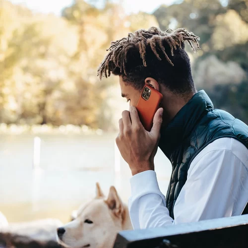 Young man with his dog sitting on a park bench talking on the phone