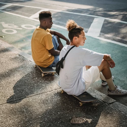 Two young men sitting on their skateboards on the sidewalk