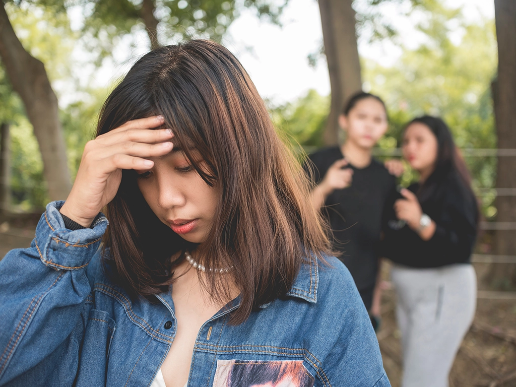 Young woman stressed out with two people talking behind her back